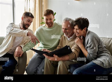 A Gay Couple Sits With Parents Looking At A Photo Album Together Stock