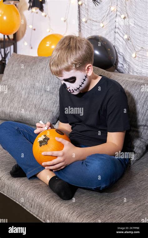 A boy in skeleton makeup paints a pumpkin for Halloween Stock Photo - Alamy