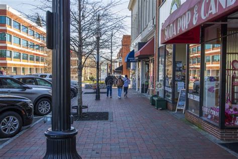 People Walking Along A Red Brick Sidewalk Lined With Shops Restaurants