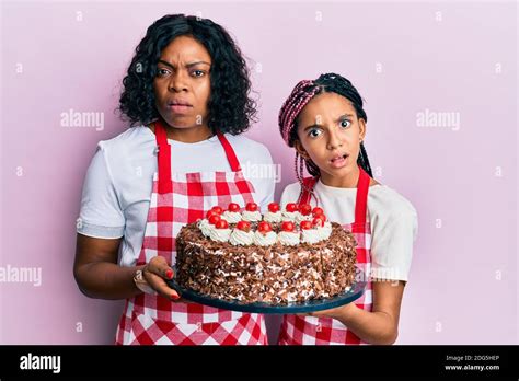 Beautiful African American Mother And Daughter Wearing Baker Apron Holding Homemade Cake In