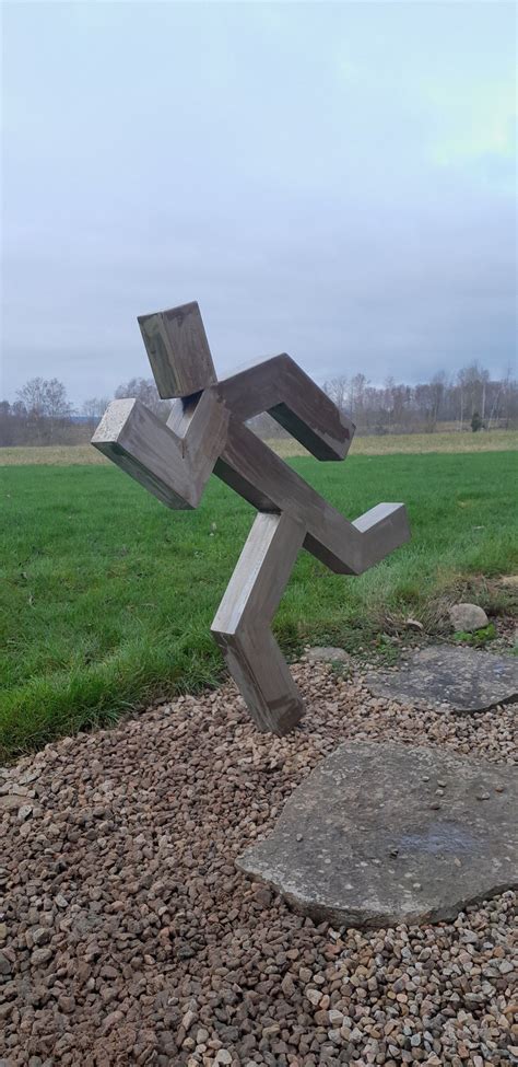 A Wooden Sculpture Sitting On Top Of A Pile Of Rocks Next To A Lush