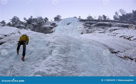 Male Mountain Guide Rappelling Off A Steep Frozen Waterfall After An