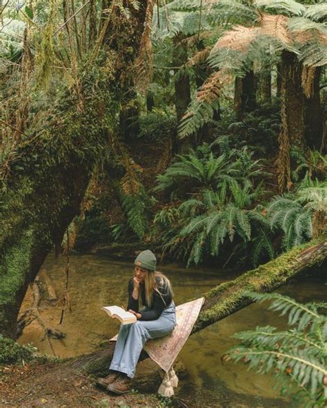 A Woman Sitting On A Log In The Middle Of A Forest Reading A Book While