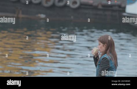 Cute Girl Sitting On Wooden Pier With Picture And Drinking Coffee From