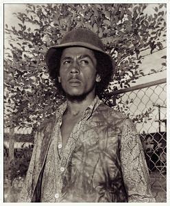 a black and white photo of a man wearing a hat in front of a fence