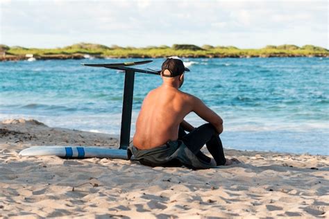 Homem sentado ao lado de sua prancha de surfe ao ar livre Foto Grátis