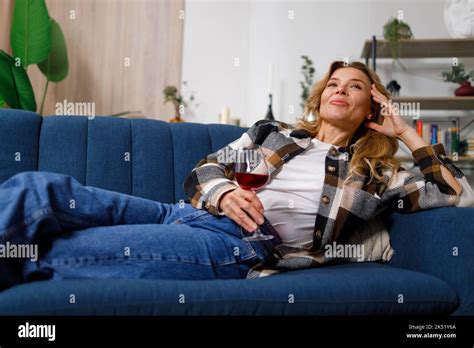 Mature Woman Drinks Red Wine From Glass Sitting On A Couch Indoors Female Spending Her Free Day