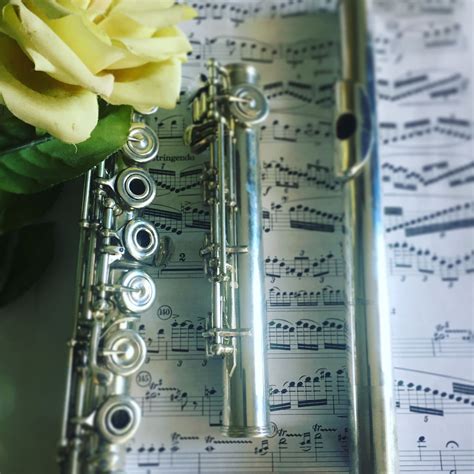 A Flute Resting On Top Of Sheet Music With A Yellow Rose In The Foreground