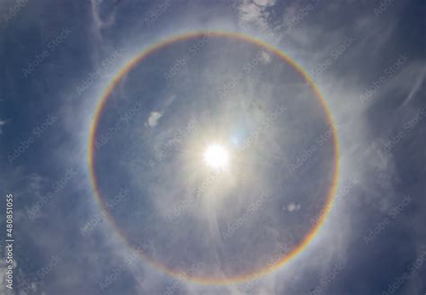 circular rainbow halo around the sun among blue sky and white clouds. Stock Photo | Adobe Stock