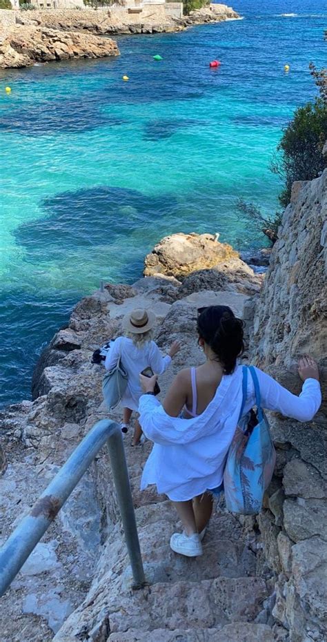 A Woman Is Walking Up Some Steps Near The Water And Rocks With Her Hand