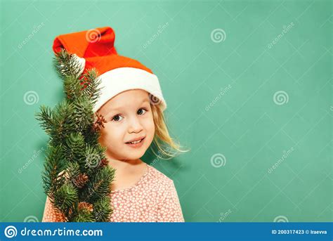 Petite Fille Dans Un Chapeau De Santa Avec Un Arbre De Sapin Sourit Sur