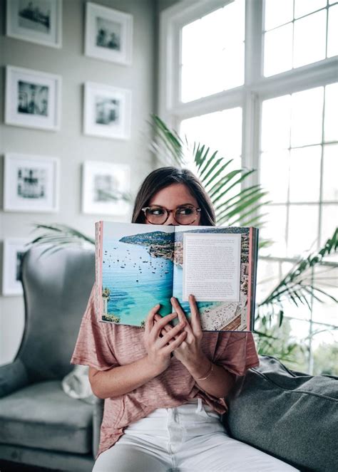 A Woman Sitting On A Couch Holding An Open Book In Front Of Her Face