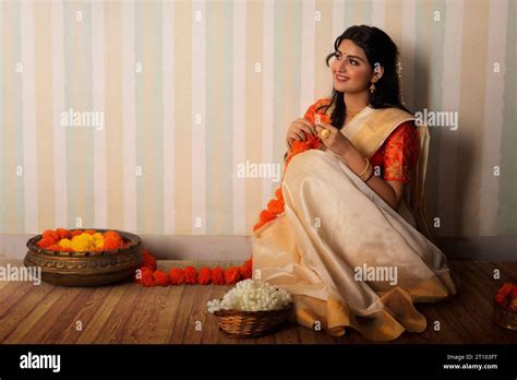 Woman In White Saree Garlanding Flowers To Celebrate Onam Stock Photo