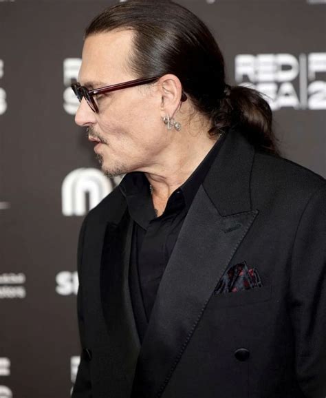 A Man With Long Hair Wearing A Black Suit And Glasses Looking Off To