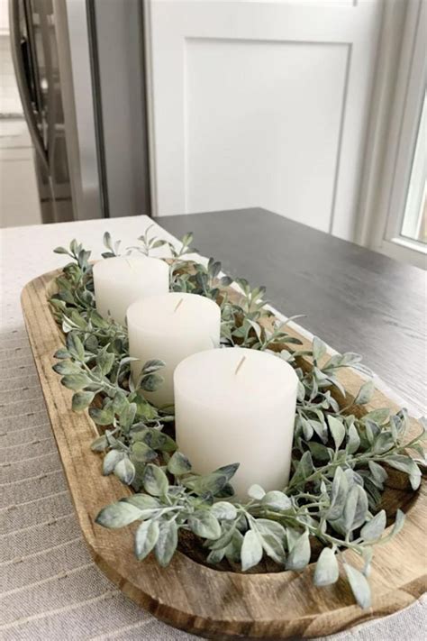 Three Candles Sitting On Top Of A Wooden Tray Filled With Greenery And