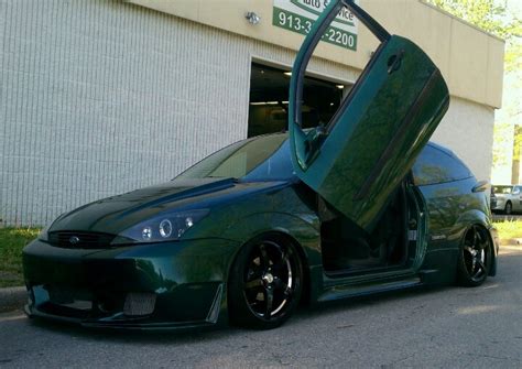 A Green Car Parked In Front Of A Building With Its Doors Open And The Door Opened