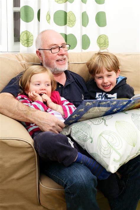 Grandpa Reading Exciting Story To His Grandchildren Sitting On Sofa