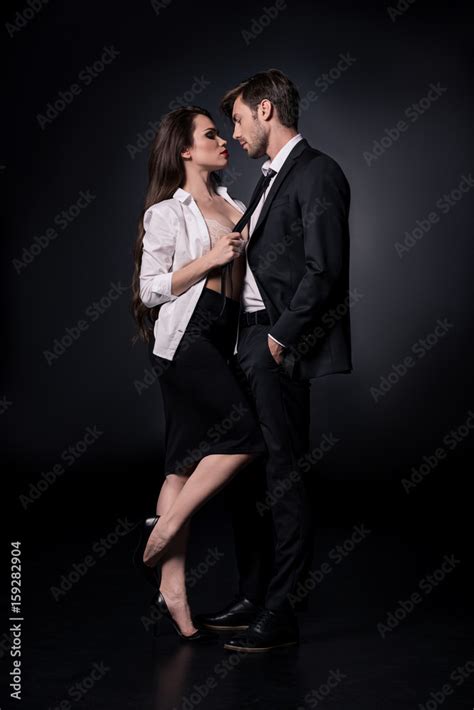 Young Sexy Woman Seducing Young Man In Suit Isolated On Black Stock