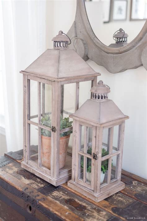 Two White Lanterns With Succulents Are Sitting On A Wooden Table In