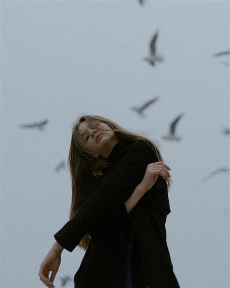 A Woman Standing In Front Of A Flock Of Birds With Her Eyes Closed And