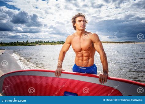 Surfer Male With A Muscular Body With His Surfboard At The Beach Stock