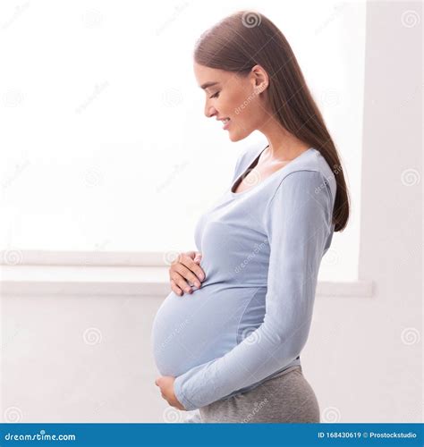 Happy Pregnant Lady Touching Belly Standing Next To Window Indoor Stock