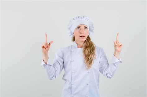 Chef Feminino Apontando Os Dedos Em Uniforme Branco E Olhando Otimista