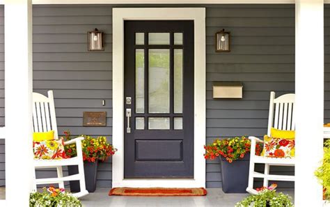 Two White Rocking Chairs Sitting In Front Of A Black Door On A Gray House With Potted Plants