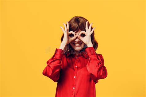 A Funny Cheerful Woman Stands In A Stylish Red Shirt On A Yellow Background And Looking Into