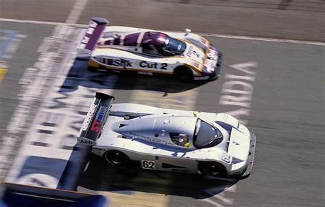 Two Race Cars Racing On A Track During The Day