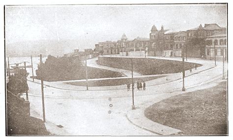 An Old Black And White Photo Of People Walking Down The Street In Front