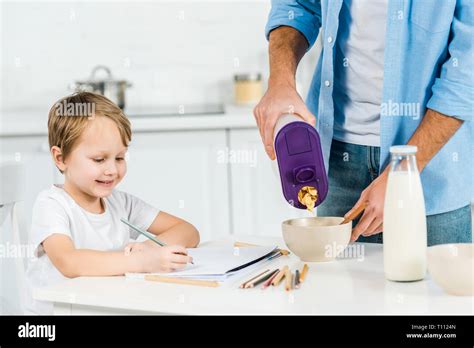 Father Pouring Cereal In Bowl While Smiling Preschooler Son Drawing