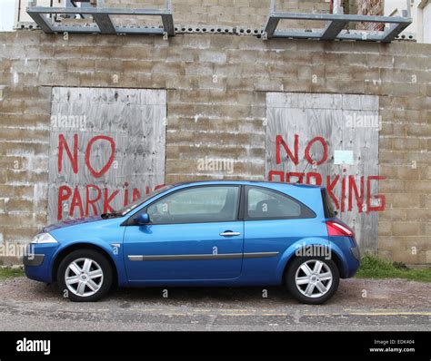 Car Parked In Front Of No Parking Painted Sign On Brick Wall And