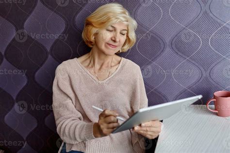 Smiling Mature Woman Using Mobile Phone While Working By Computer At Home Stock Photo