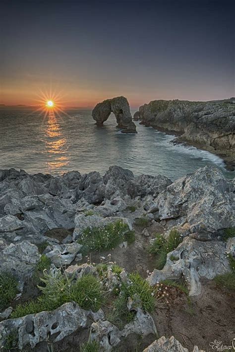 The Sun Is Setting Over The Ocean And Rocks