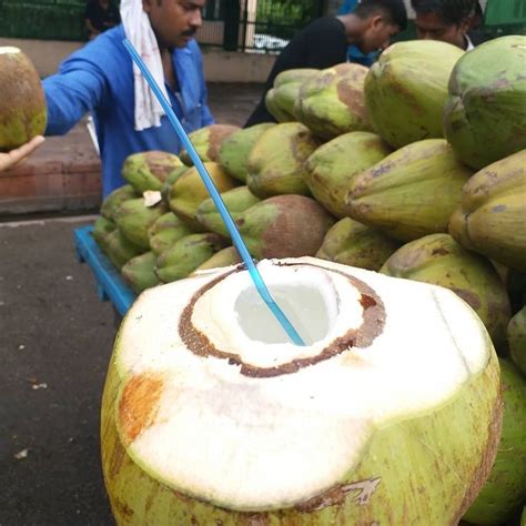 A Man Standing Next To A Pile Of Coconuts With A Blue Straw In It