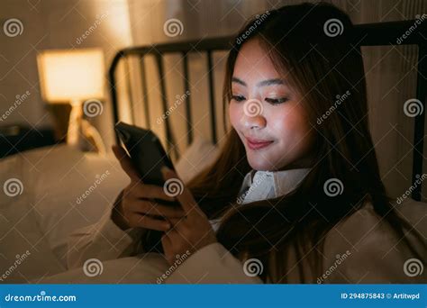 Portrait Of Asian Teen Girl Lying In Bed At Night And Using Smartphone