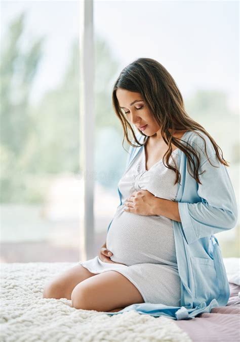 Portrait Of Young Pregnant Woman Relax Sittong In Bed And Touching Her