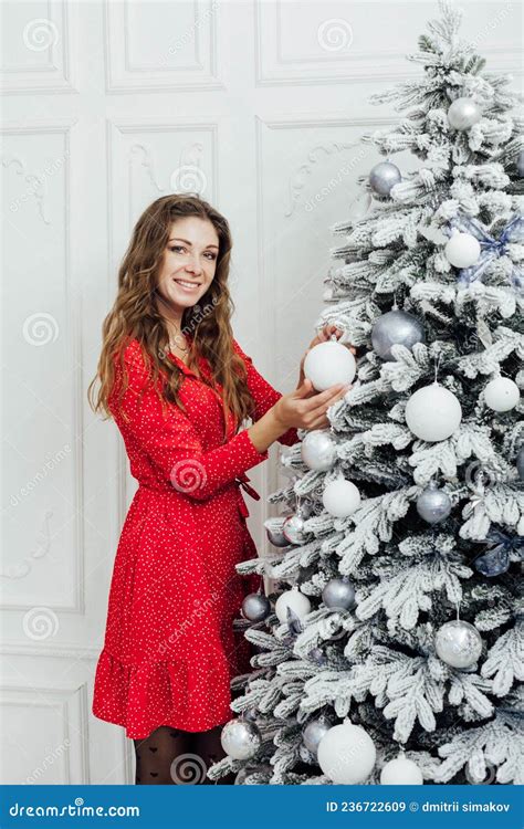 Beautiful Woman In A Red Light Dress Decorates A Christmas Tree For The