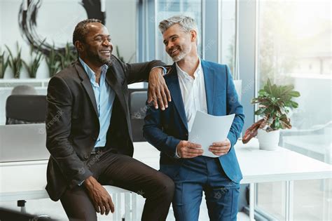 Premium Photo Two Smiling Businessmen Talking About Deal Sitting In