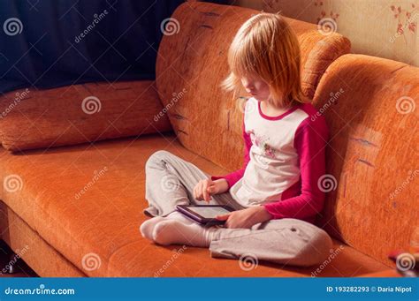 Blond Caucasian Girl Sitting On A Sofa And Reading Electronic Book