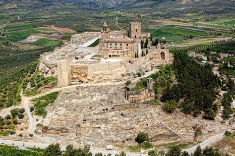 An Aerial View Of A Castle Surrounded By Hills And Trees With Mountains