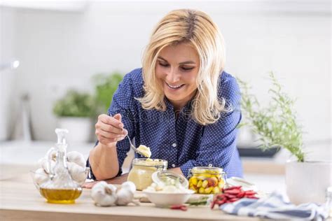 Smiling Blonde Woman Takes Spoonful Of Crushed Garlic During Preserves Making Session In The