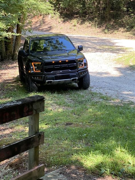 A Black Truck Parked On The Side Of A Road Next To A Wooden Fence And Trees