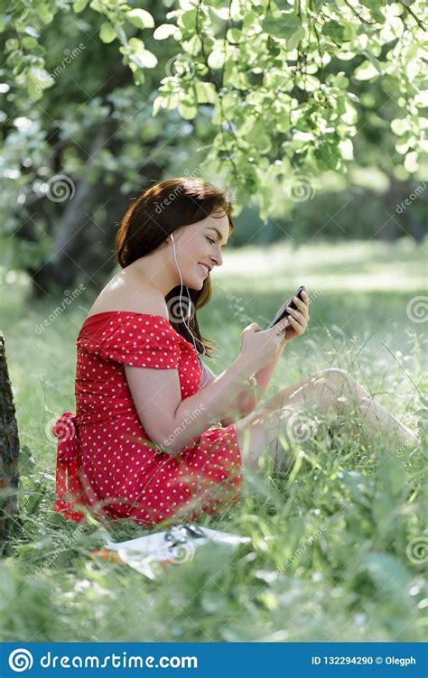 Plus Size Girl Sitting On Grass Under Tree And And Using Her Smartphone