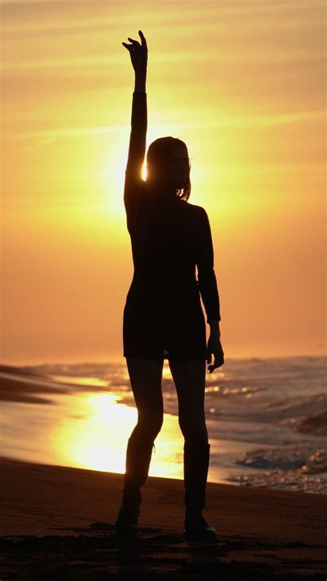 Silhouette Woman Arms Raised On Sandy Beach At Sunrise On Background