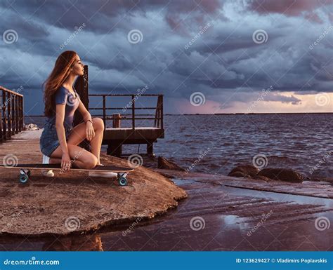 Sensual Girl Sitting On A Skateboard On The Beach Is Enjoying Amazing