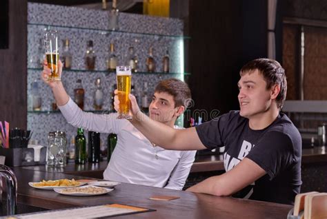 Dos Hombres Jovenes Que Aumentan Sus Cervezas En Una Tostada Foto De