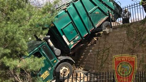 Garbage truck crashes, hangs over retaining wall in Mass.