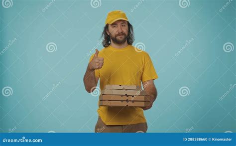 Delivery Man In Yellow Uniform Holding A Stack Of Pizza Boxes And Shows